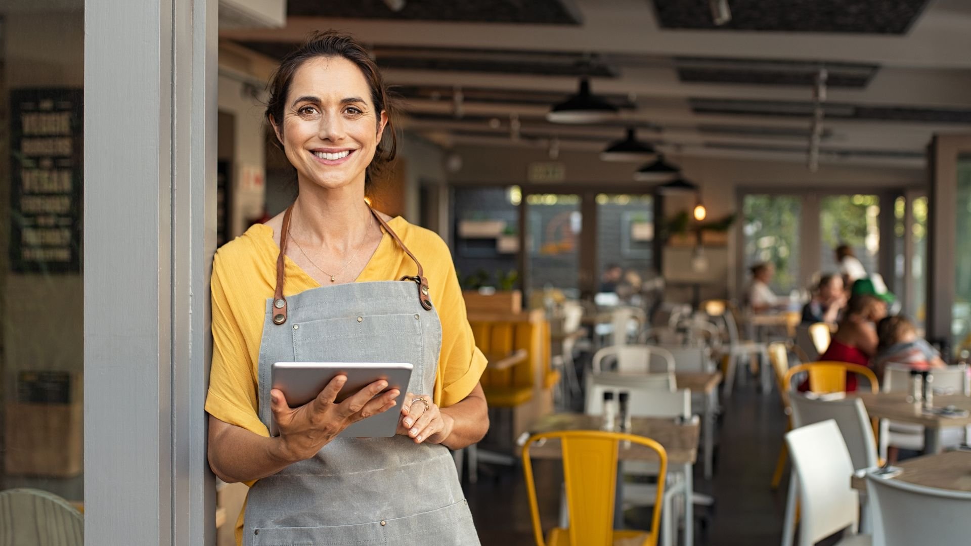 Smiling cafe worker in yellow shirt and gray apron holding tablet